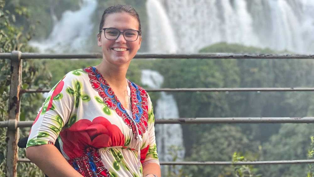 A girl smiling in front of a waterfall sitting in a wheelchair.