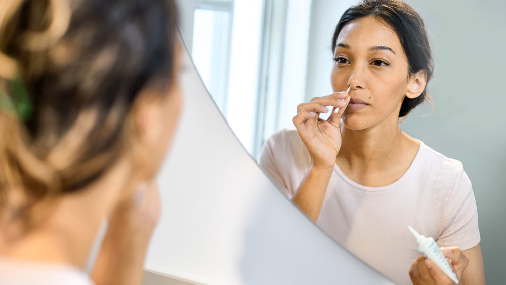 woman performing  antimicrobial nose rinsing at home in front of bath mirror