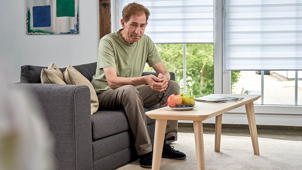 older thin man sits thoughtfully on a sofa