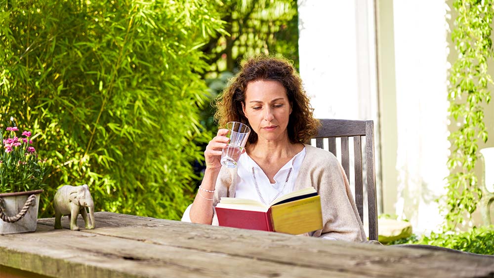 A woman sits on a chair, reads a book and holds a glass in her hand