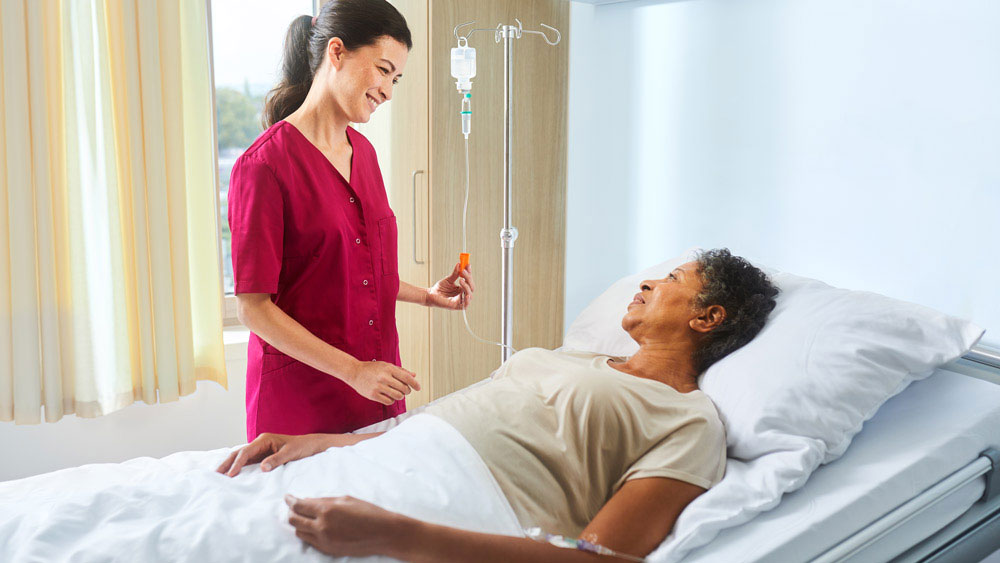 Nurse with ecoflac plus on an infusion stand talking to a patient lying in bed