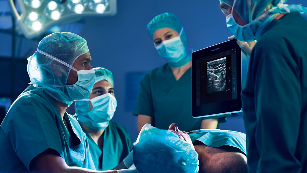 Medical staff observe an ultrasound-guided infraclavicular plexus block on a monitor in the operating room